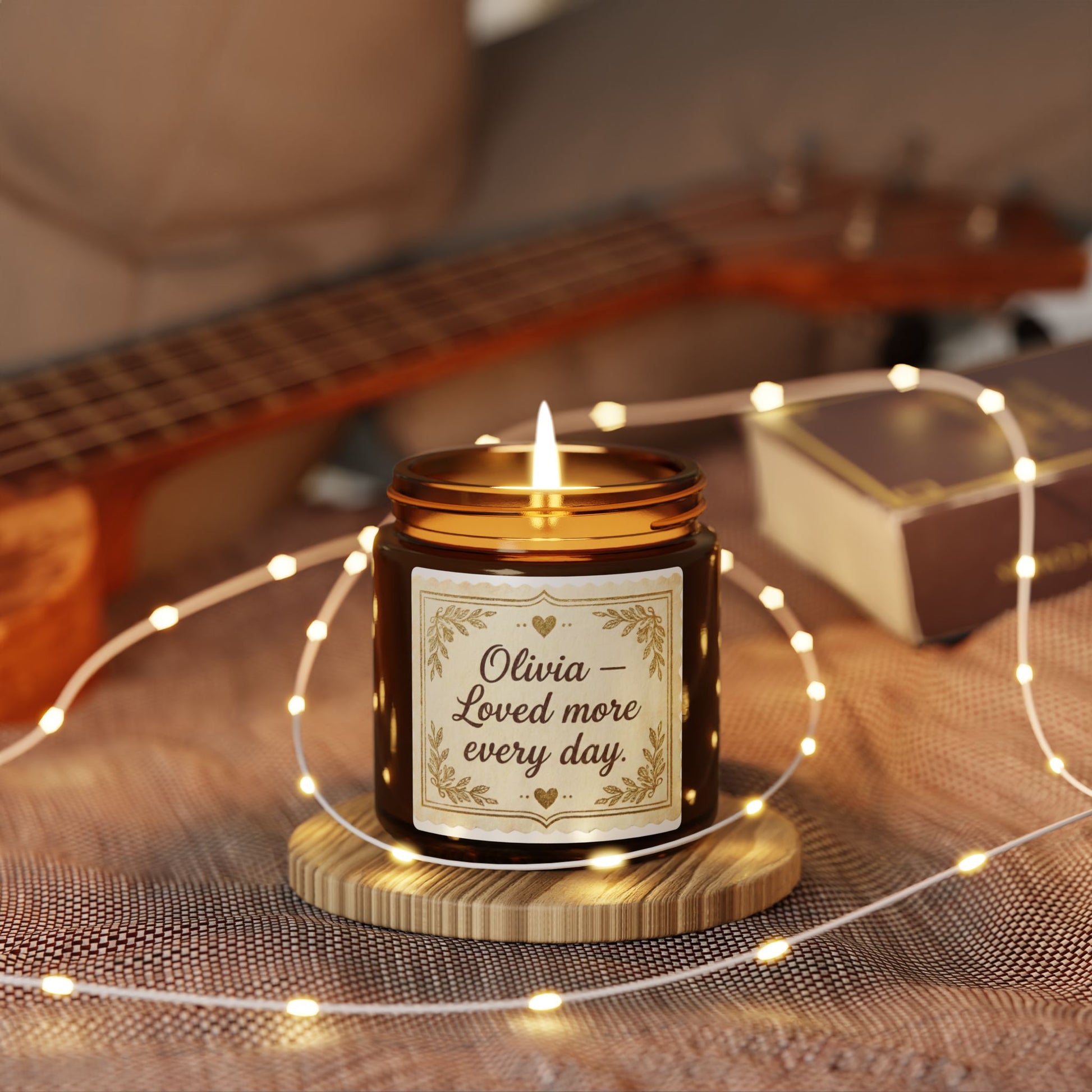 Lit amber jar candle with 'Olivia – Loved more every day' label, cozy decor, string lights