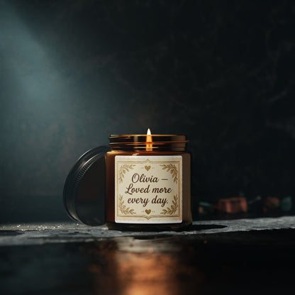 Amber glass candle with 'Olivia – Loved more every day' label on dark stone background